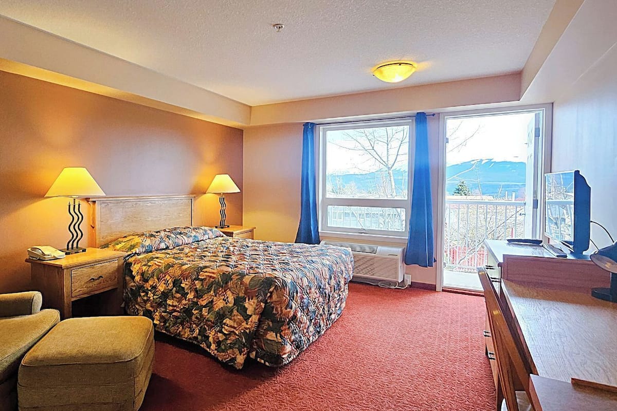 A hotel room with a bed, two bedside lamps, a chair, a desk, and a window with curtains.