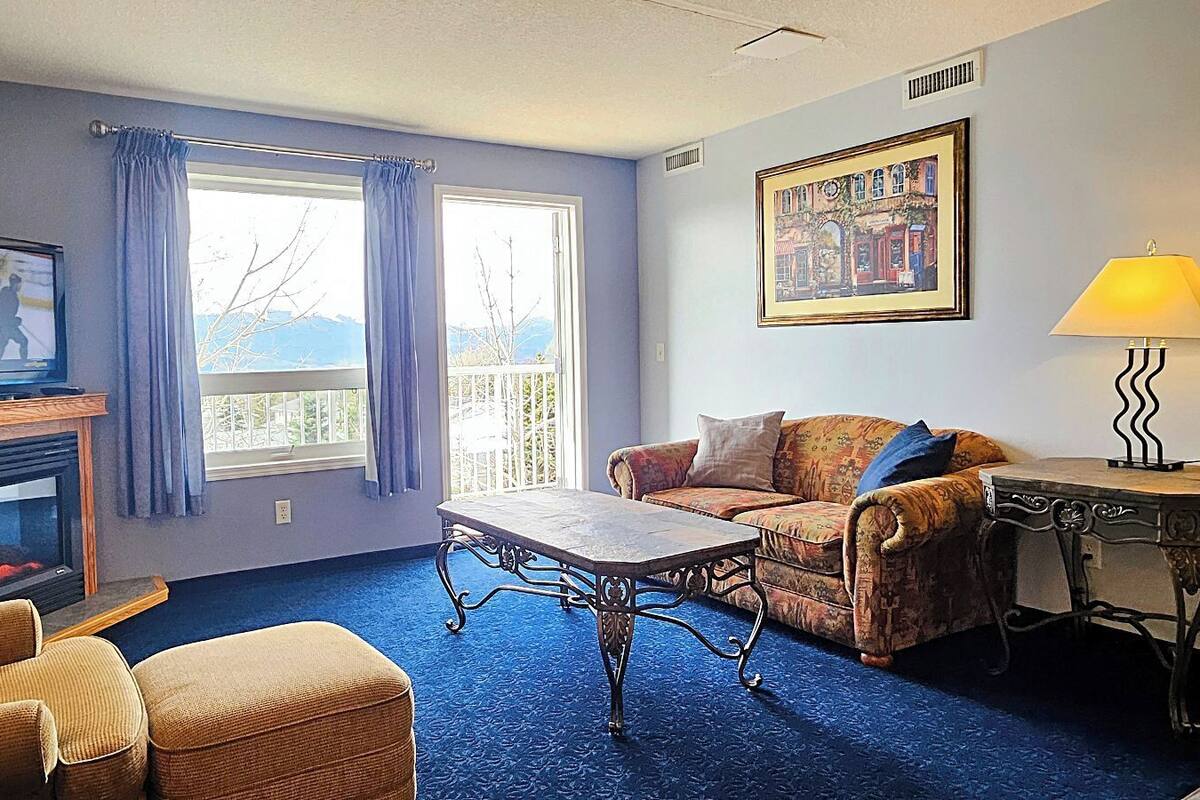 A room with a fireplace, a television, a sofa, a table, and a painting on the wall.