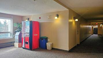 A hallway with a vending machine, trash bins, and wall-mounted lights.
