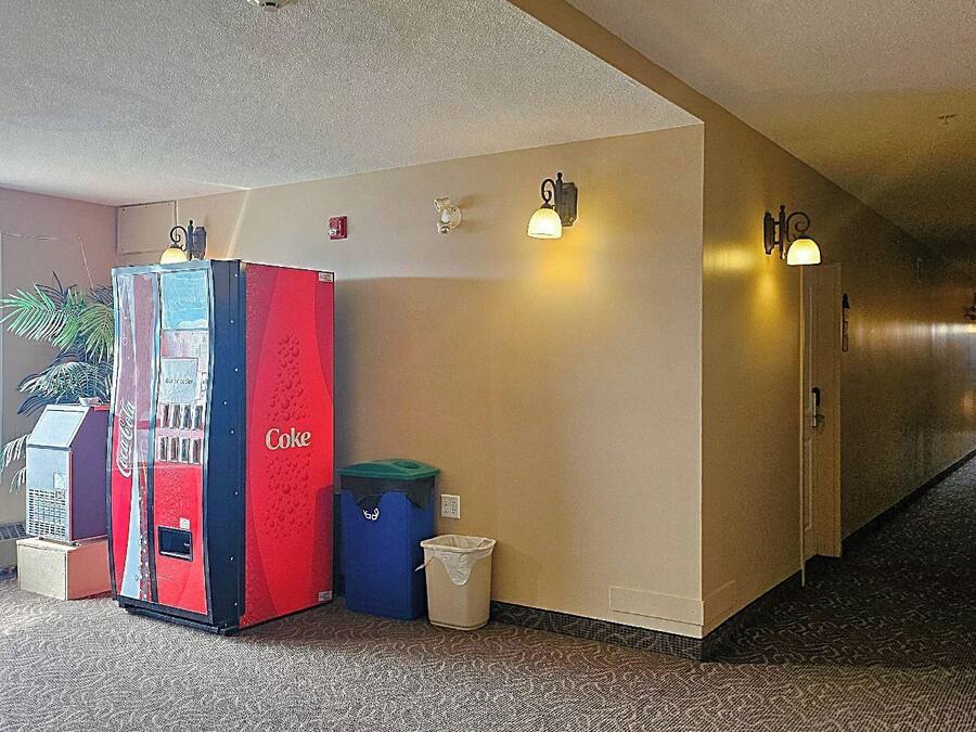 A hallway with a vending machine, trash bins, and wall-mounted lights.