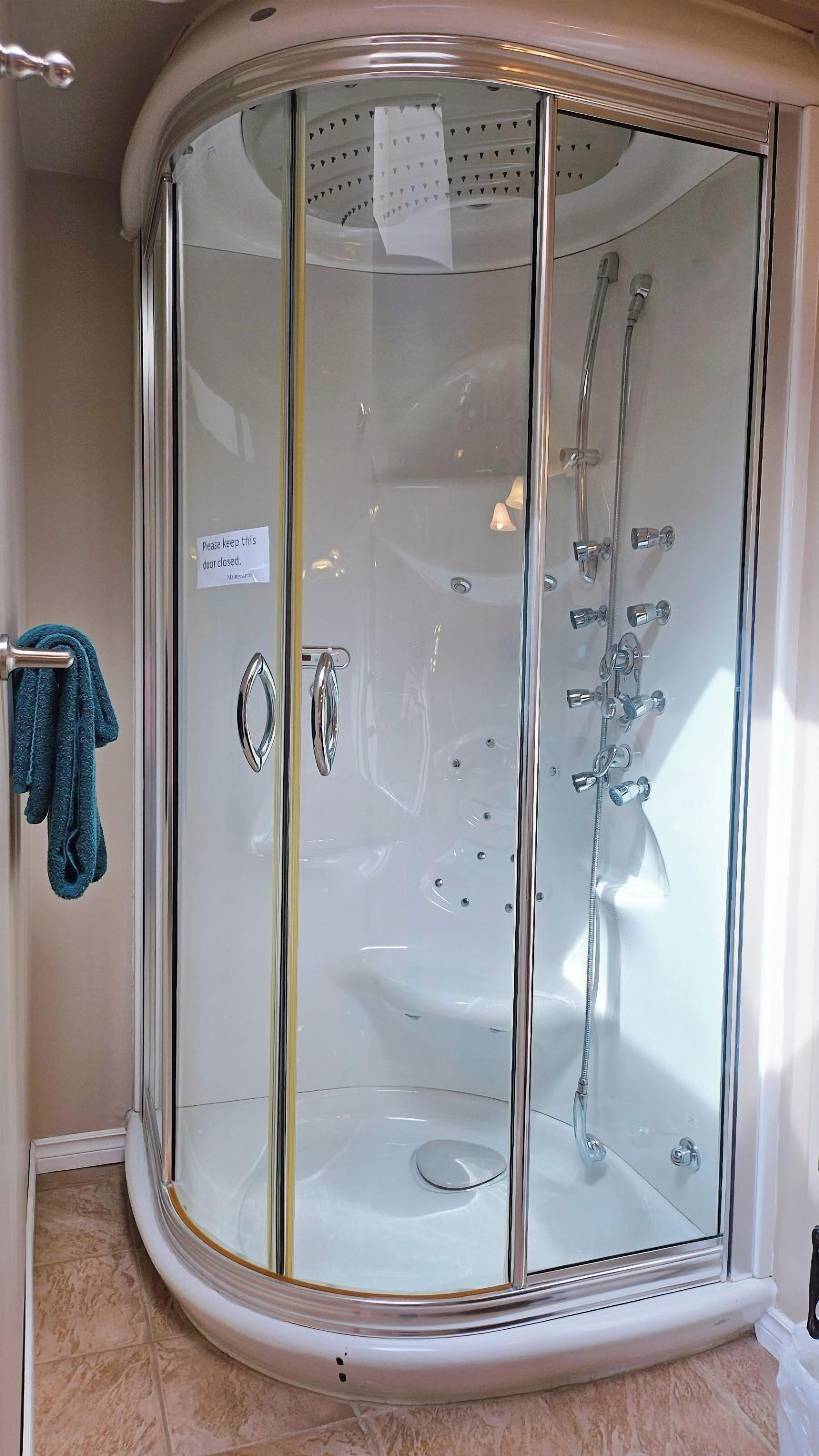 A glass-enclosed walk-in shower with a towel rack and a sign instructing to keep the door closed.