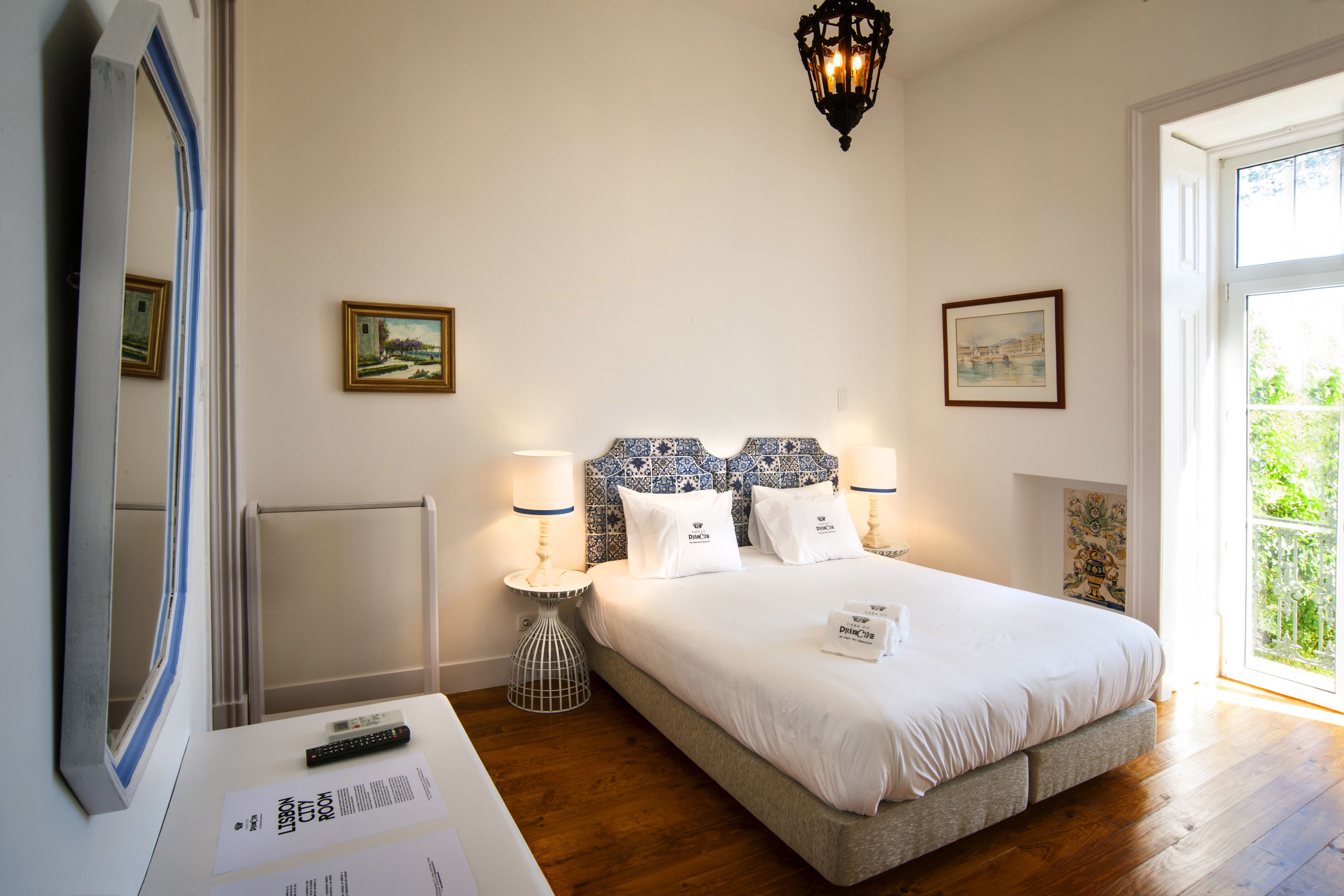 Ein Hotelzimmer mit einem großen Bett, zwei Nachttischen mit Lampen, einem Spiegel und gerahmten Bildern an den Wänden.