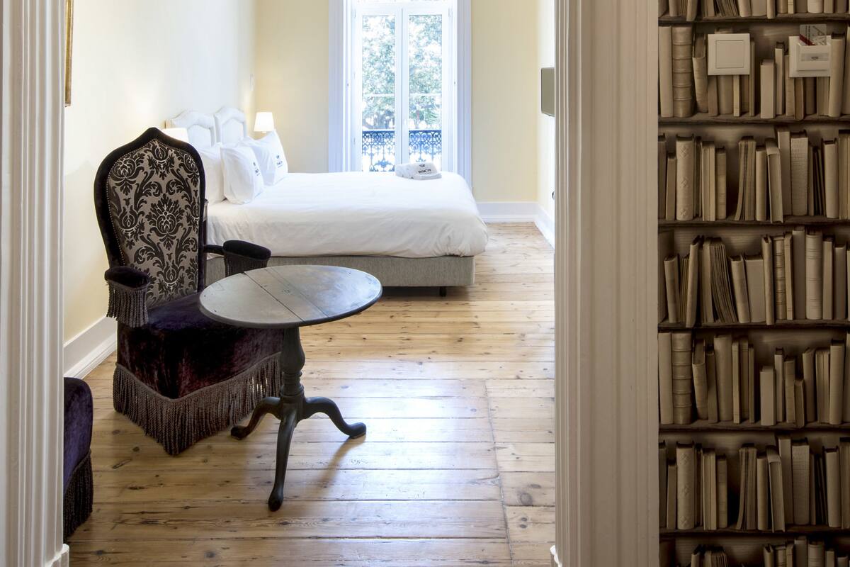 A bedroom with a large bed, a chandelier, a chair, and a bookshelf.