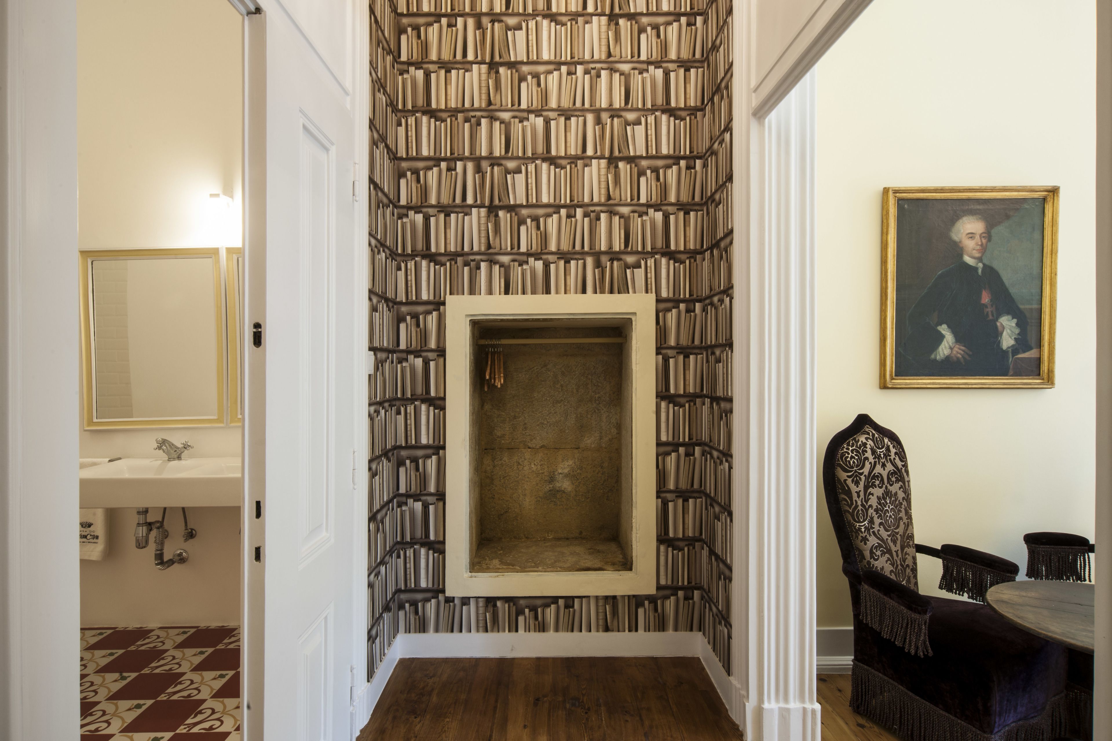 Un couloir avec un mur entier recouvert d’étagères à livres, une cheminée, un coin repas avec une table et des chaises, et un tableau accroché au mur.