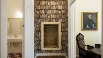 Un couloir avec un mur entier recouvert d’étagères à livres, une cheminée, un coin repas avec une table et des chaises, et un tableau accroché au mur.