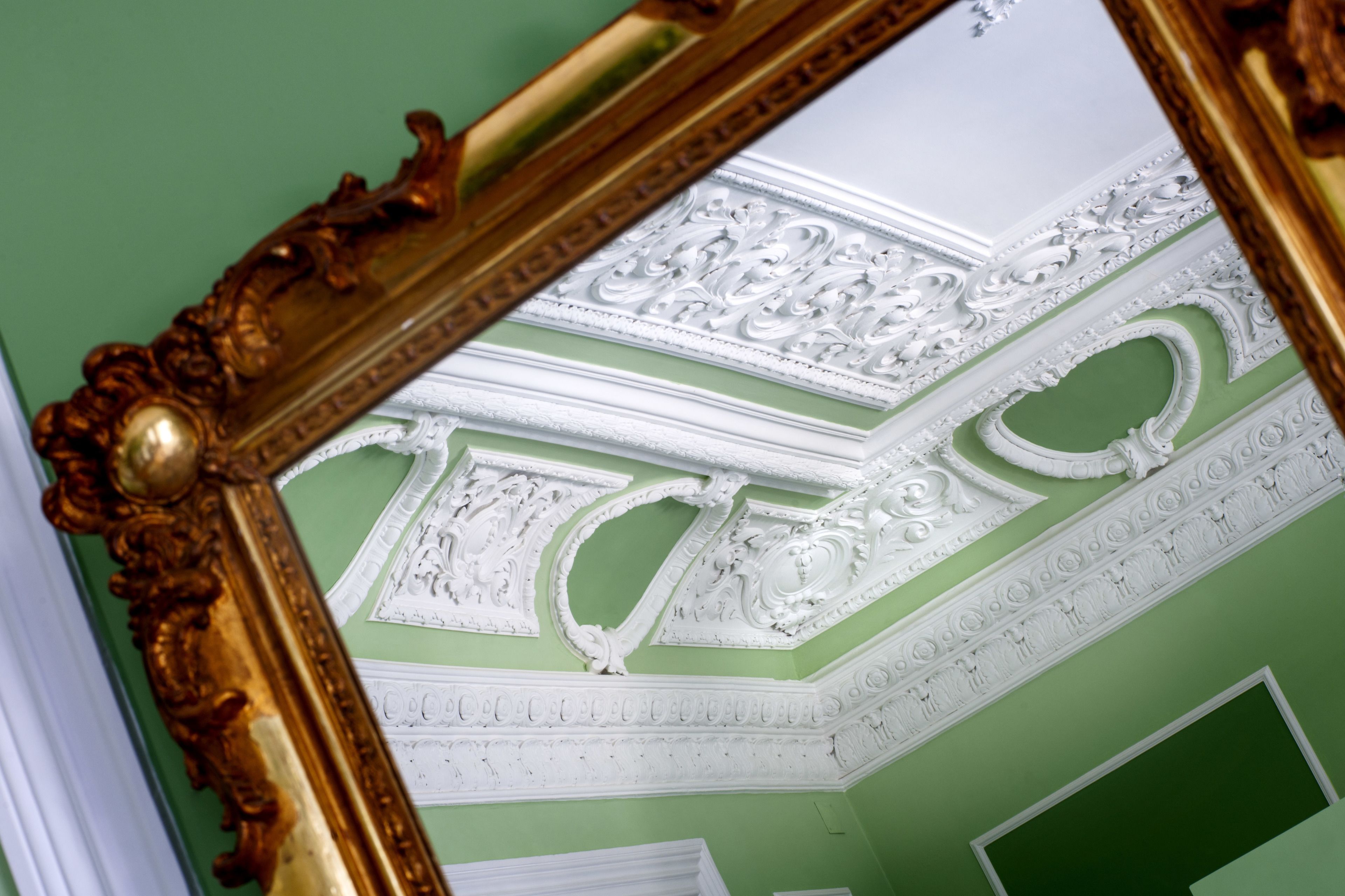 A room with ornate ceiling moldings and a gold-framed mirror.
