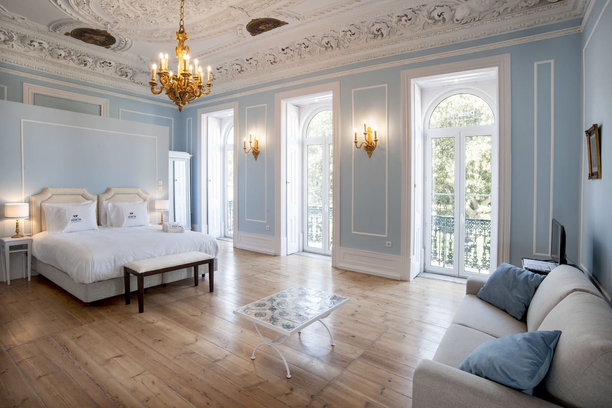 A spacious bedroom with a large bed, a bench, a small table, and a sofa.