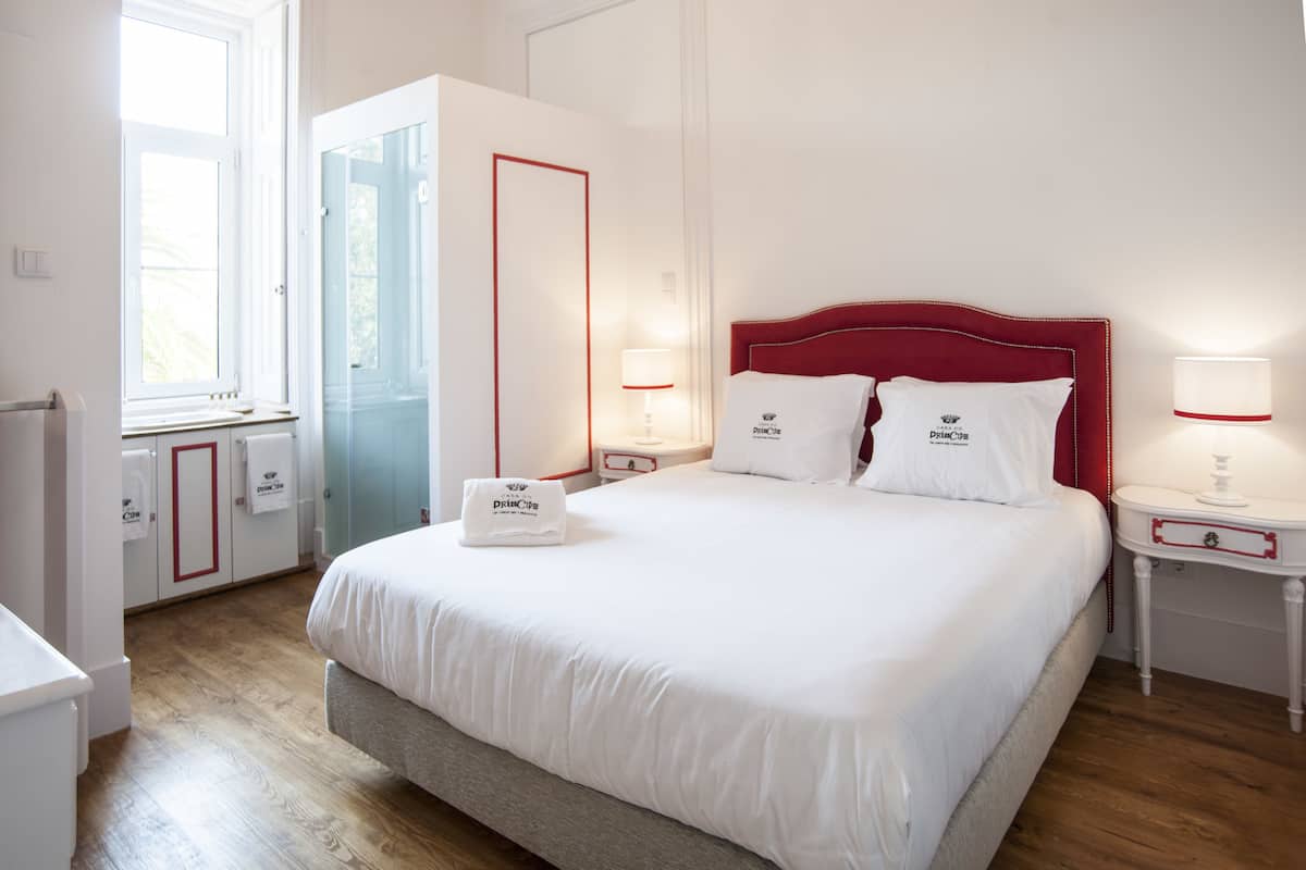 A neatly arranged hotel room with a large bed, bedside tables with lamps, a wardrobe, and a window providing natural light.