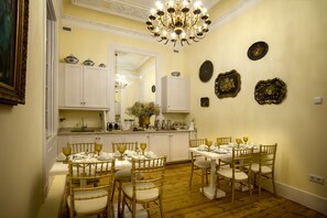 Un comedor con una mesa dispuesta para seis personas, rodeada por seis sillas. Un candelabro cuelga del techo, y hay platos decorativos en la pared.