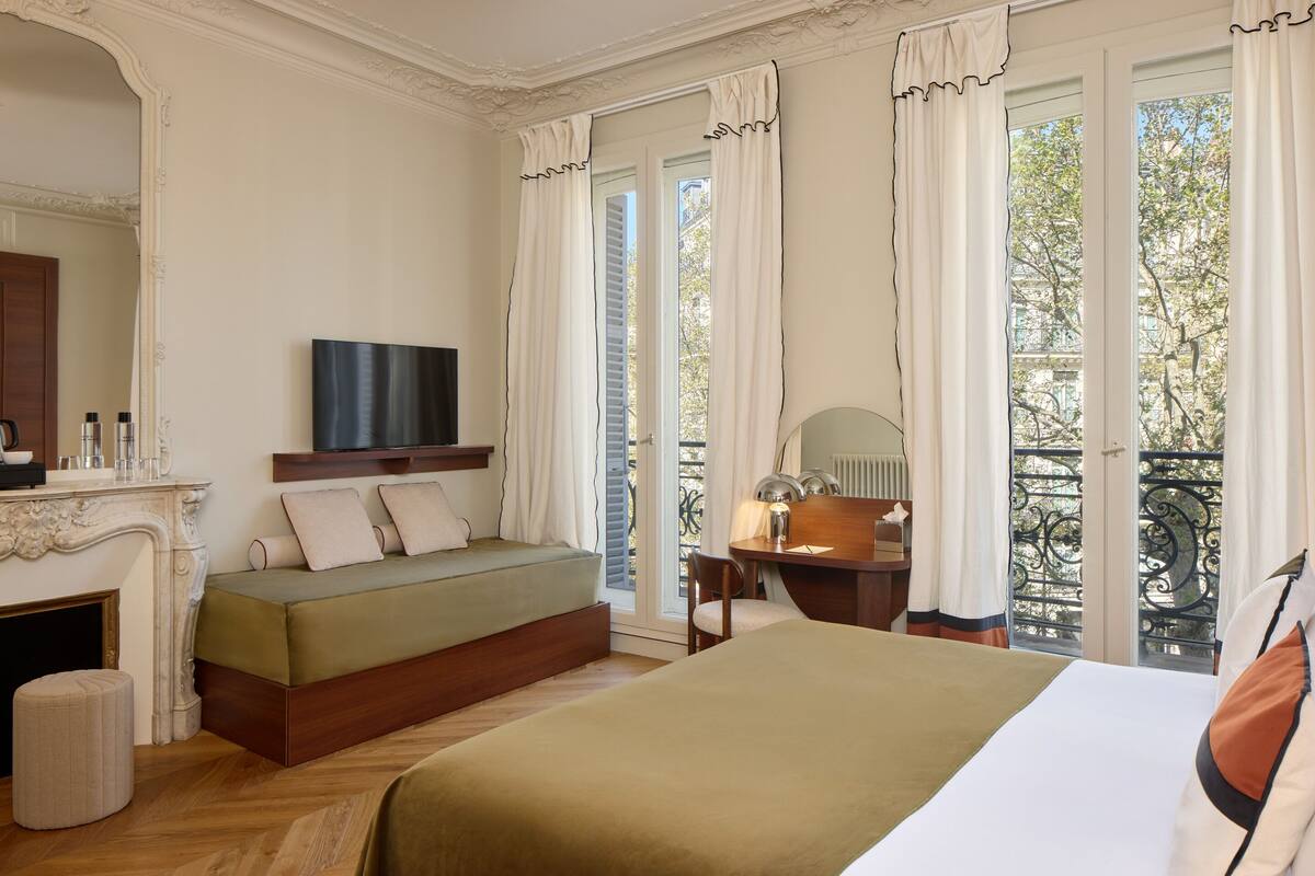 A bedroom with a bed, a television, a fireplace, and a balcony with a view.