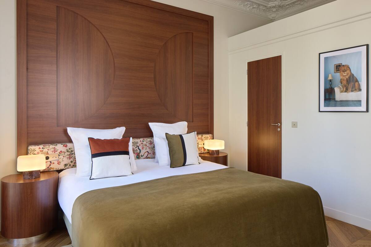 A hotel room with a large bed, two bedside tables, a wooden headboard, a framed picture on the wall, and a door.