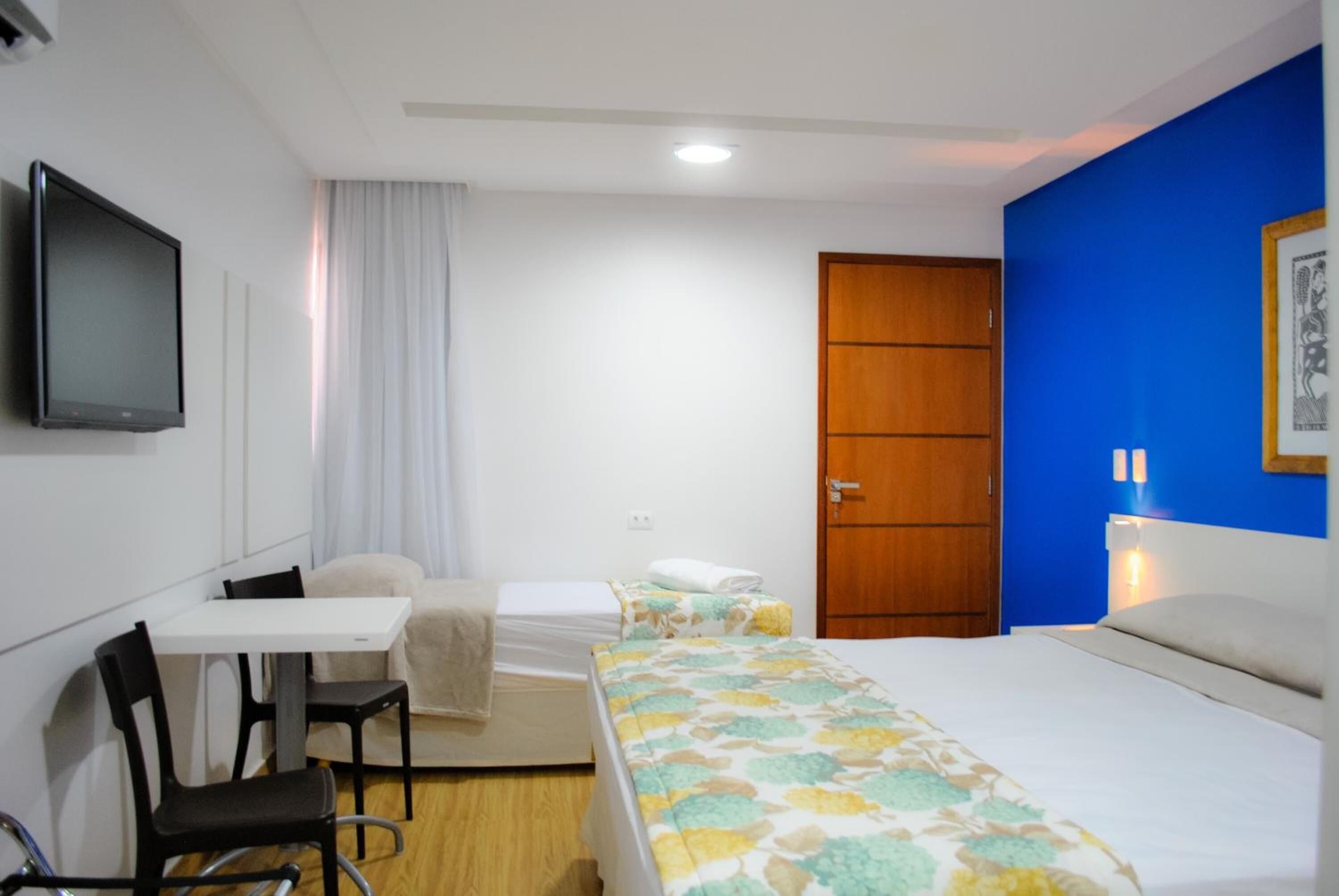 A hotel room with a bed, a desk with a chair, a television, and a wardrobe.