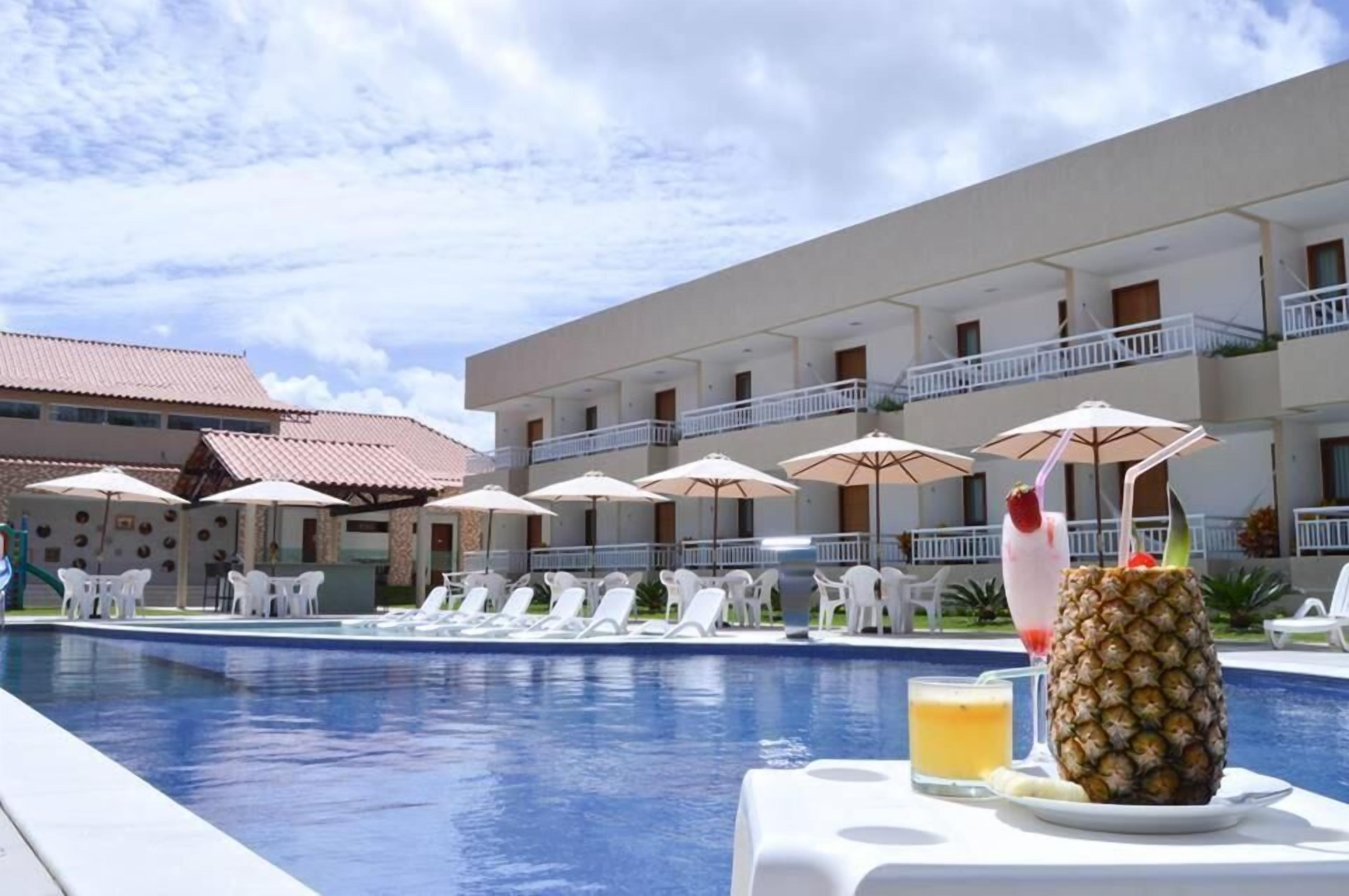 A hotel pool area with sun loungers, umbrellas, and a pineapple drink on a table.