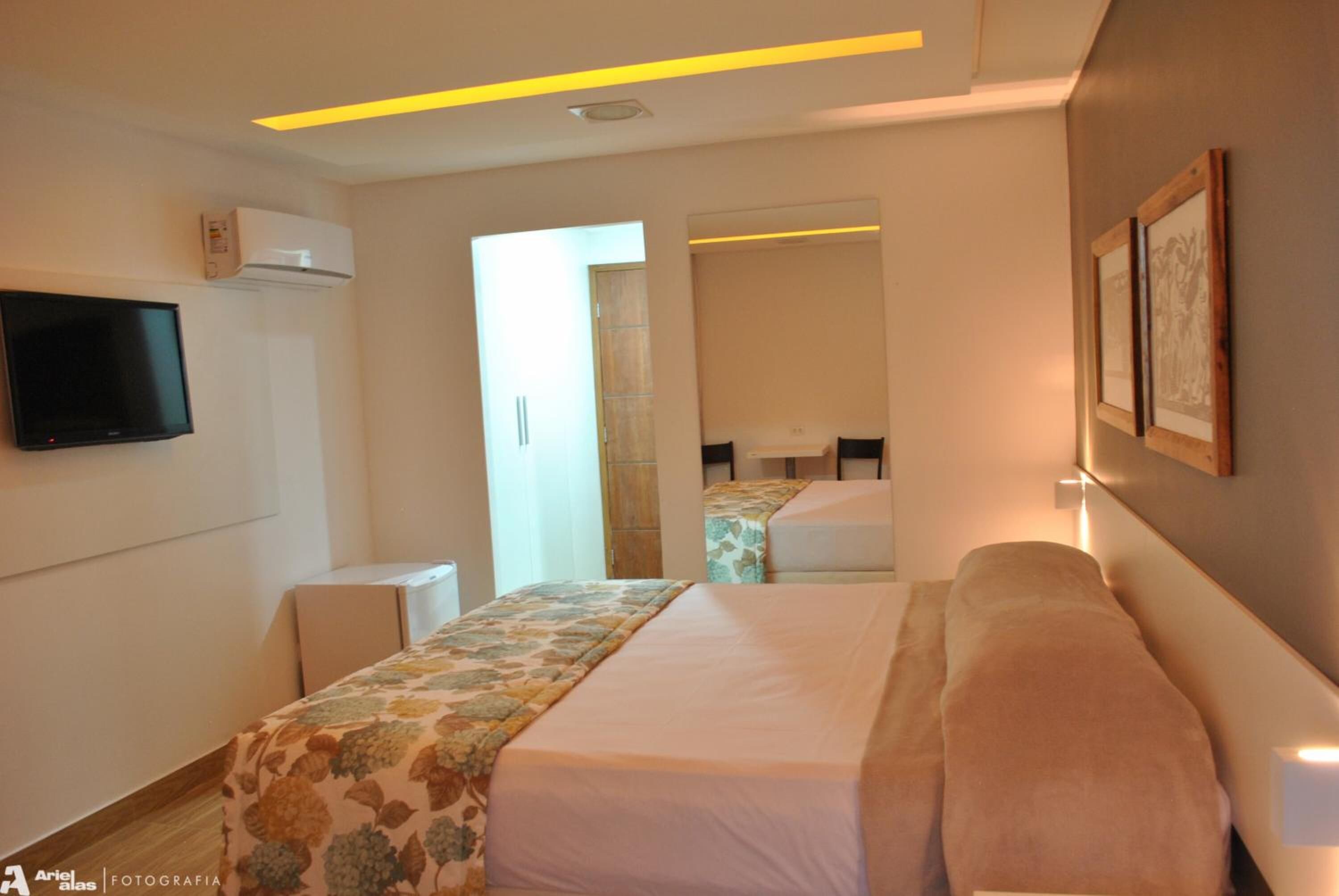 A hotel room with a bed, a flat-screen TV, an air conditioning unit, and a mirror.