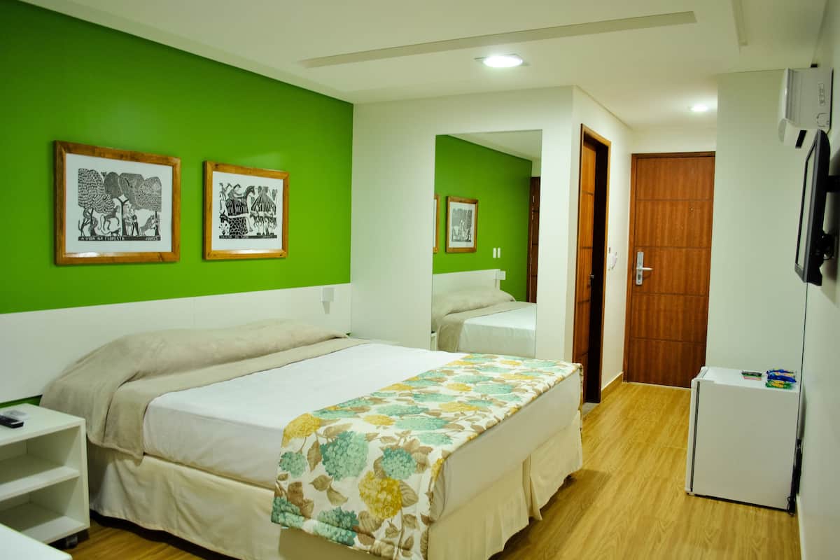 A hotel room with a bed, a small desk, a wardrobe, and a refrigerator.