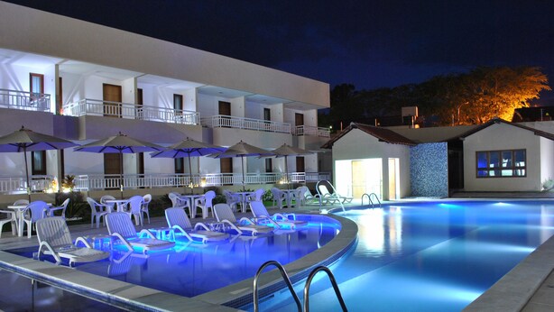 A swimming pool with lounge chairs and umbrellas, a building with balconies, and a small house with a tiled exterior. - Porto da Serra Hotel (Gravata)
