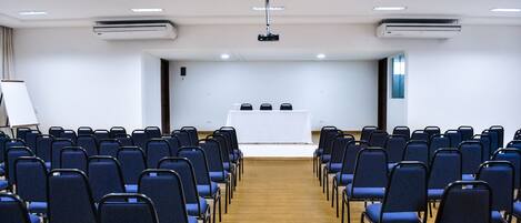 A conference room with rows of chairs facing a white table with three chairs.