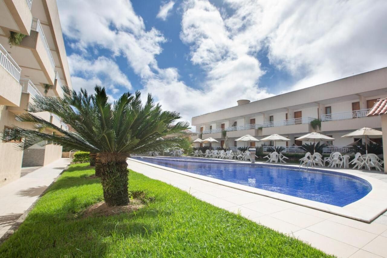 A swimming pool with lounge chairs and umbrellas, surrounded by a building with balconies and a palm tree.
