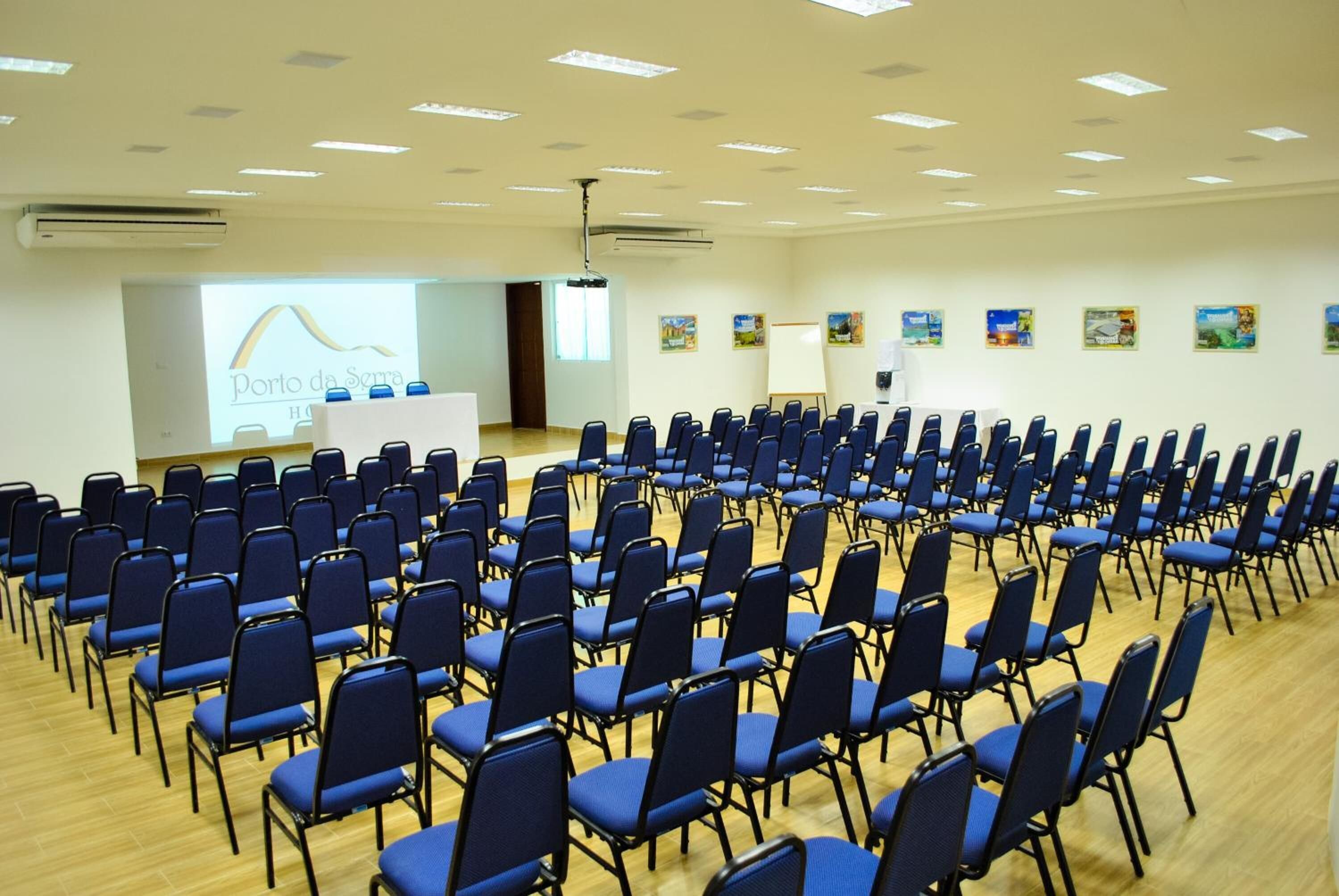 A conference room with rows of blue chairs, a podium, and a presentation screen.