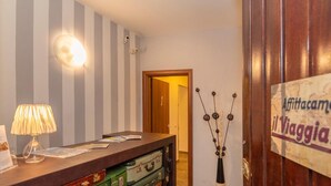 Un espace d’accueil avec un mur à rayures, une lampe, un bureau avec des papiers, une porte en bois et une enseigne indiquant « Affittacamere il Viaggiatore ».