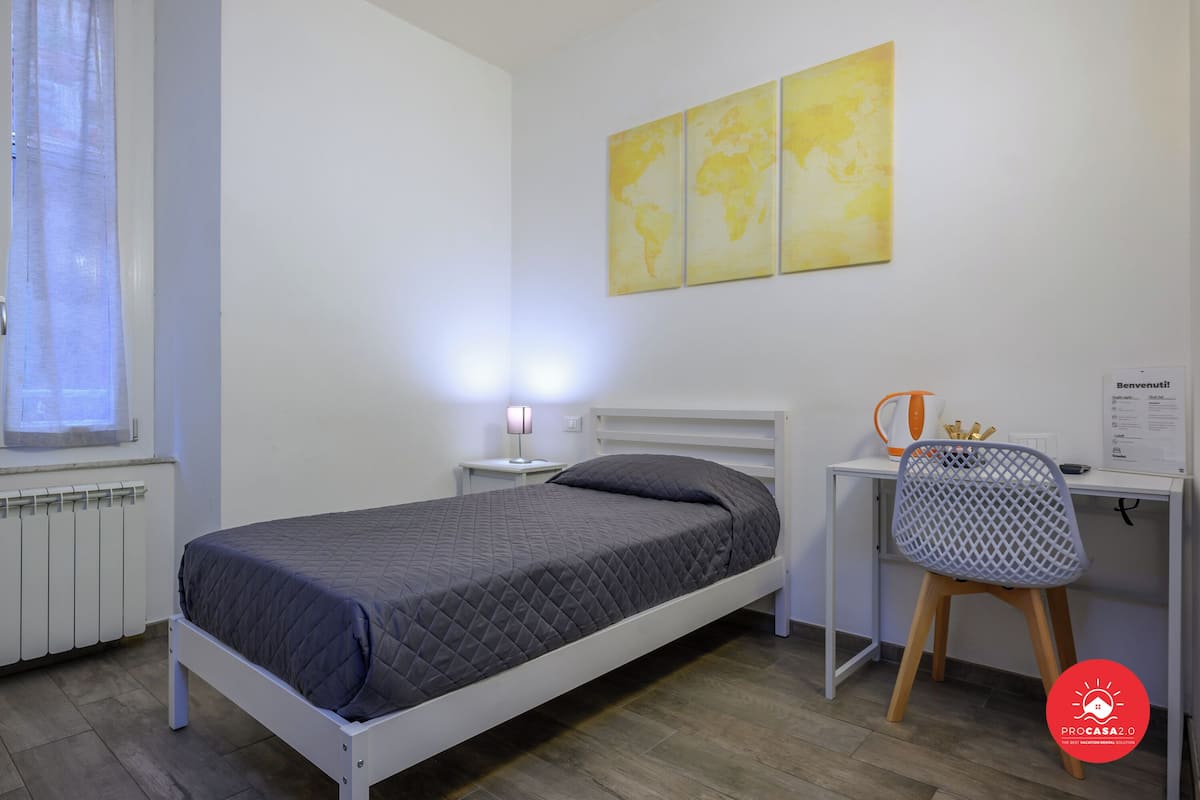 Ein Schlafzimmer mit einem Bett, einem Schreibtisch, einem Stuhl, einem Fenster und einer Wand mit drei gelben Bildern.