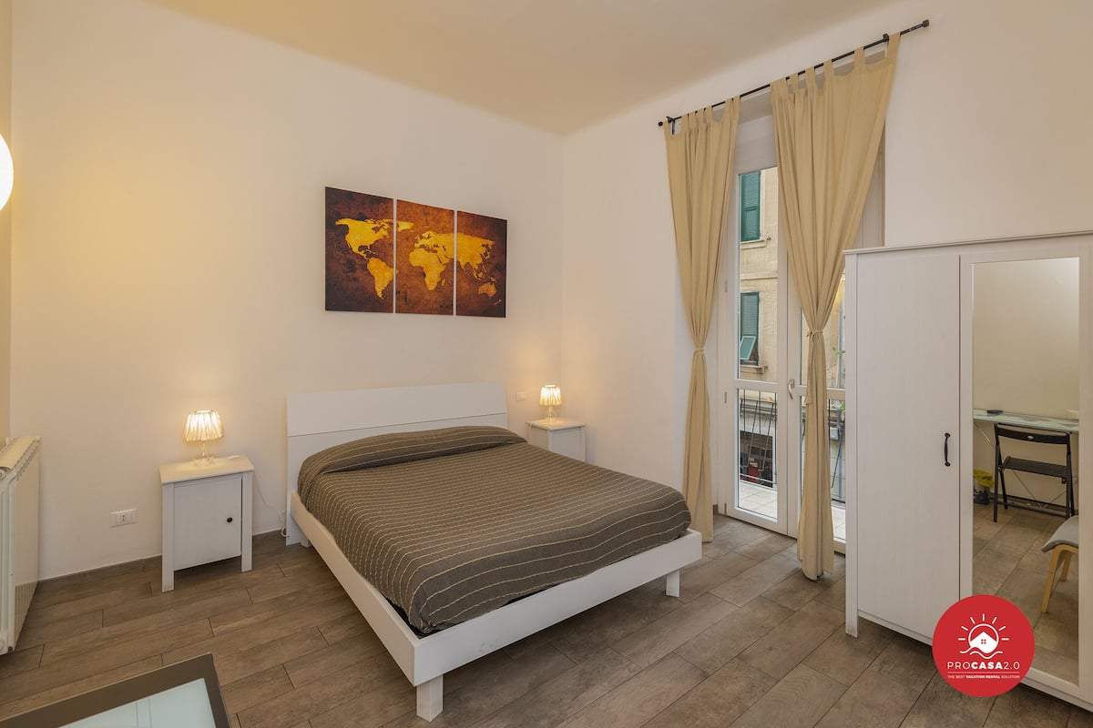 Ein Schlafzimmer mit einem Bett, Nachttischlampen, einer Weltkarte als Wandbild, einem Kleiderschrank und einem Schreibtisch.