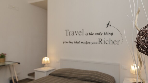 Un lit bien fait, avec une couvre-lit à rayures, un mur orné d’une citation sur le voyage et des lampes de chevet.