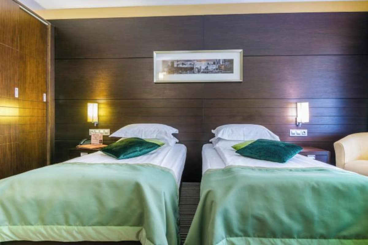 A hotel room with two beds, a dark wooden headboard, a framed picture, bedside lamps, and a chair.