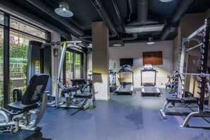 Un gimnasio con diversos equipos de ejercicio, ventanas amplias y vistas a zonas verdes.