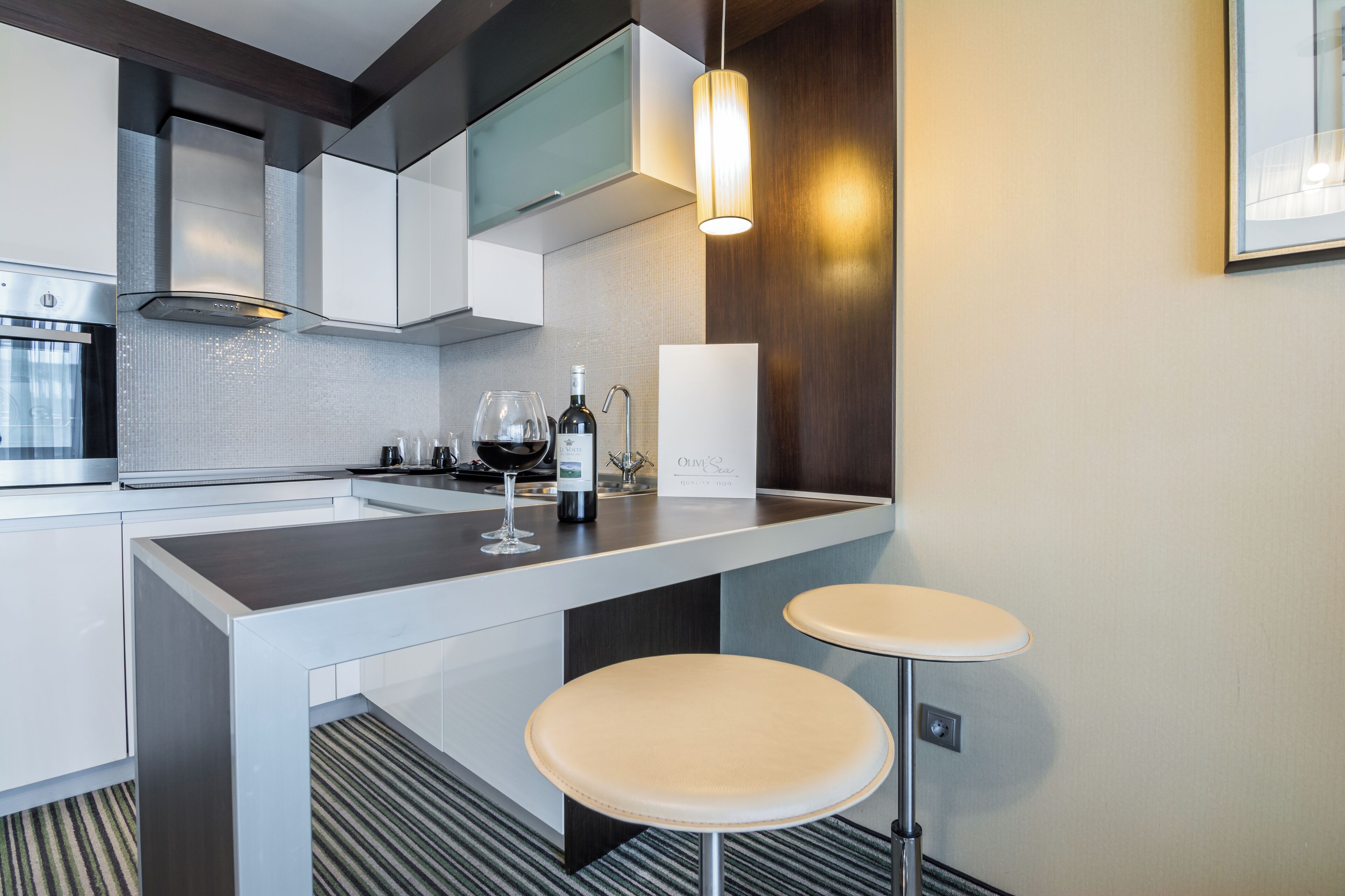 A modern kitchen with a central island, two bar stools, a wine bottle, and a wine glass.