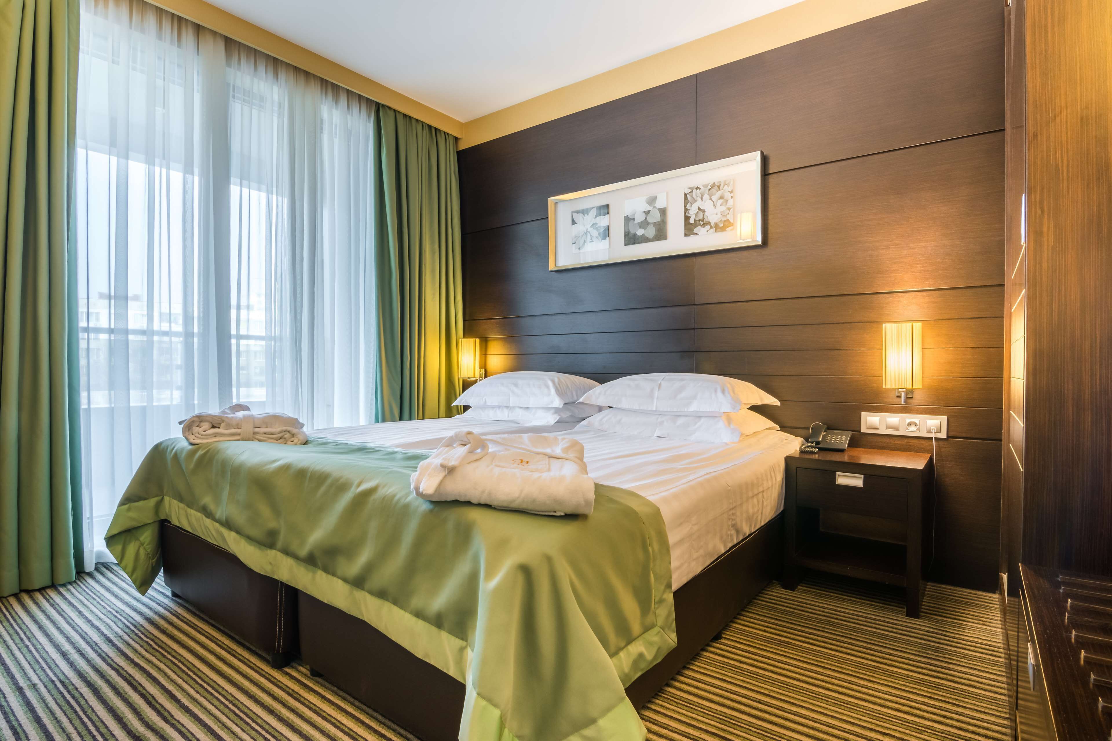Una habitación de hotel con una cama bien hecha, una mesita de noche con una lámpara y un cuadro en la pared.