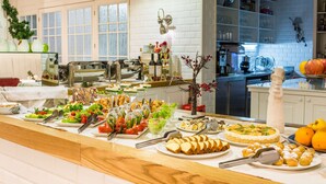 Un bufé con diversos platos y bebidas, una zona de cocina con electrodomésticos y una presentación de frutas.