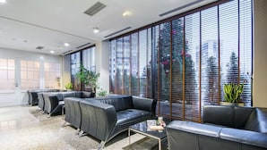 Un área de espera moderna con sofás de cuero, una mesa de centro de vidrio y ventanas amplias con persianas.