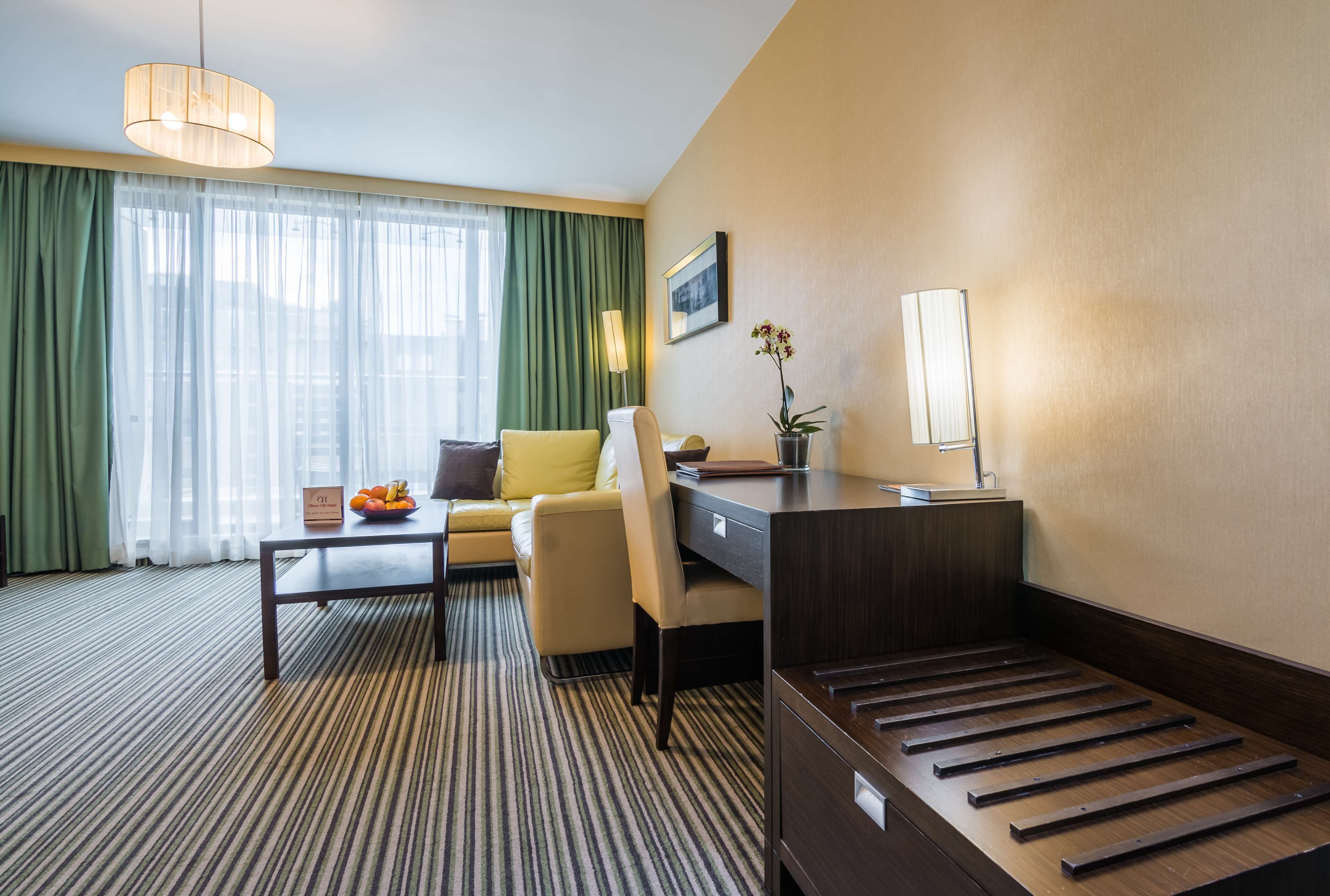 A hotel room with a sofa, a desk, a lamp, a small table with fruit, and a bed with a wooden frame.