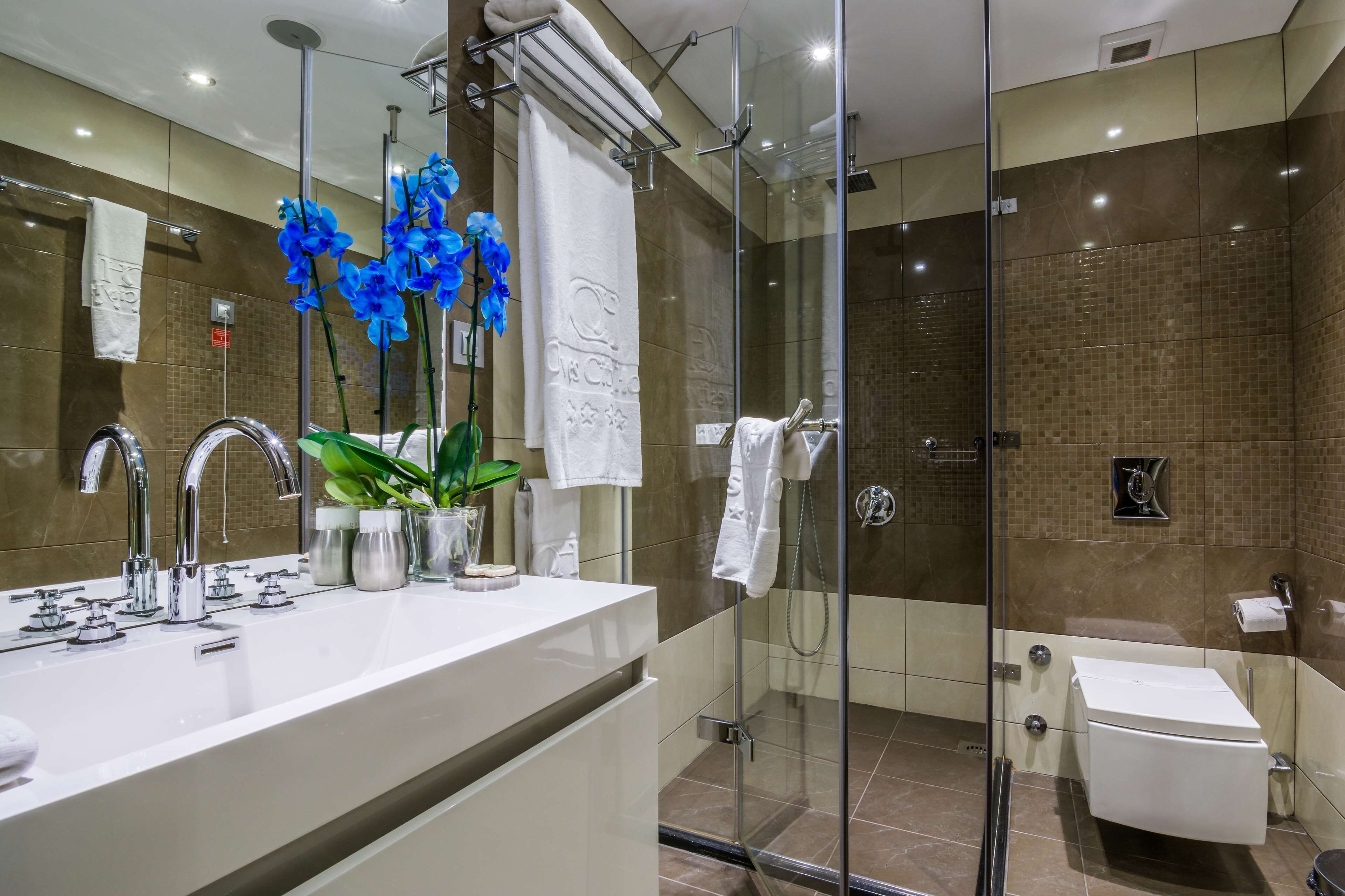 Un baño moderno con ducha envuelta en vidrio, un lavamanos blanco con múltiples grifos y un espejo grande.