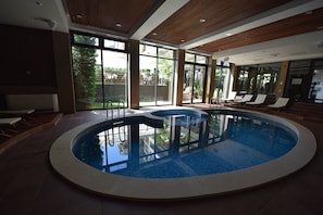 Ein großes Hallenbad mit klaren Glaswänden, Liegestühlen und Blick ins Freie.