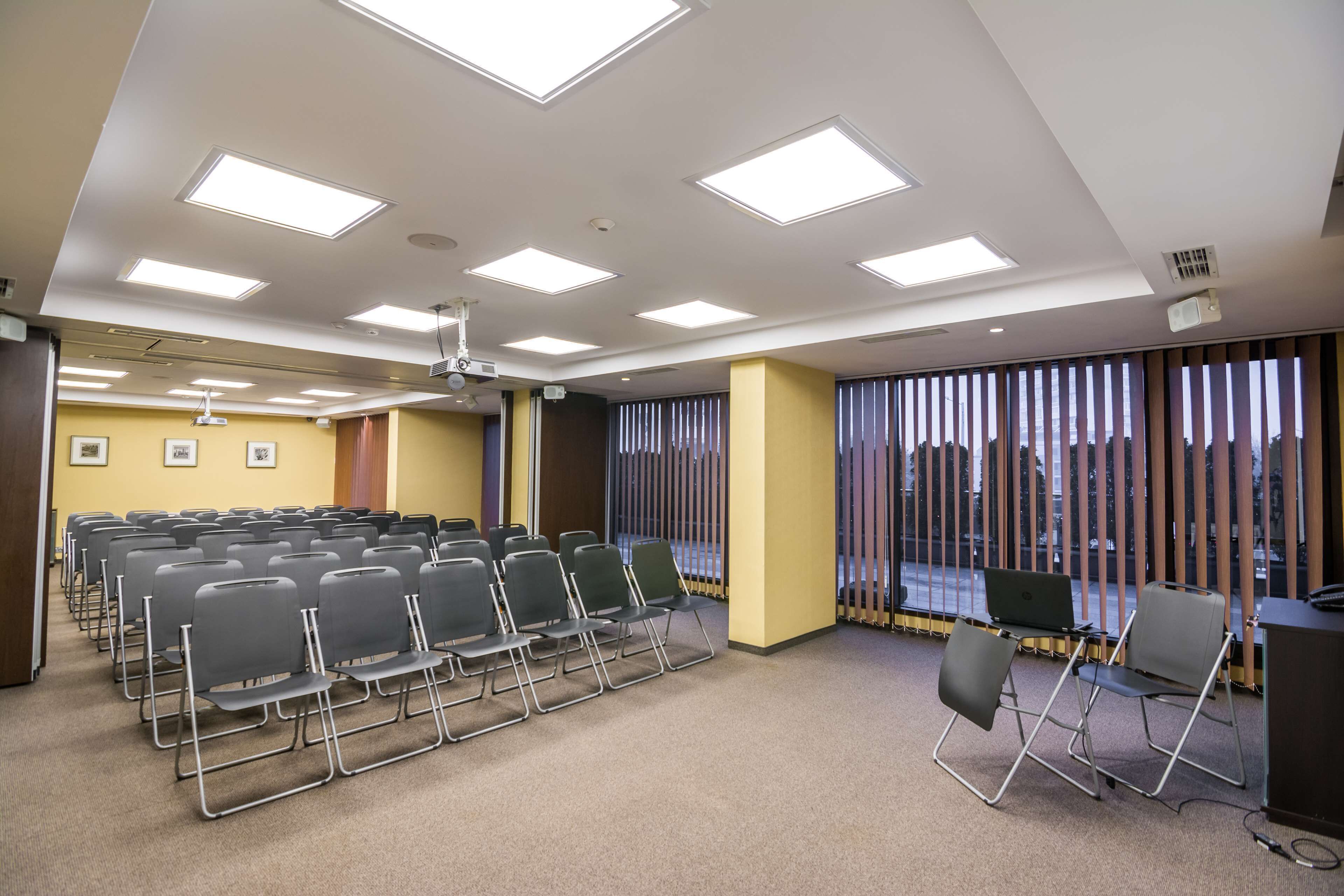 A conference room with rows of chairs, a projector, and a large window with blinds.