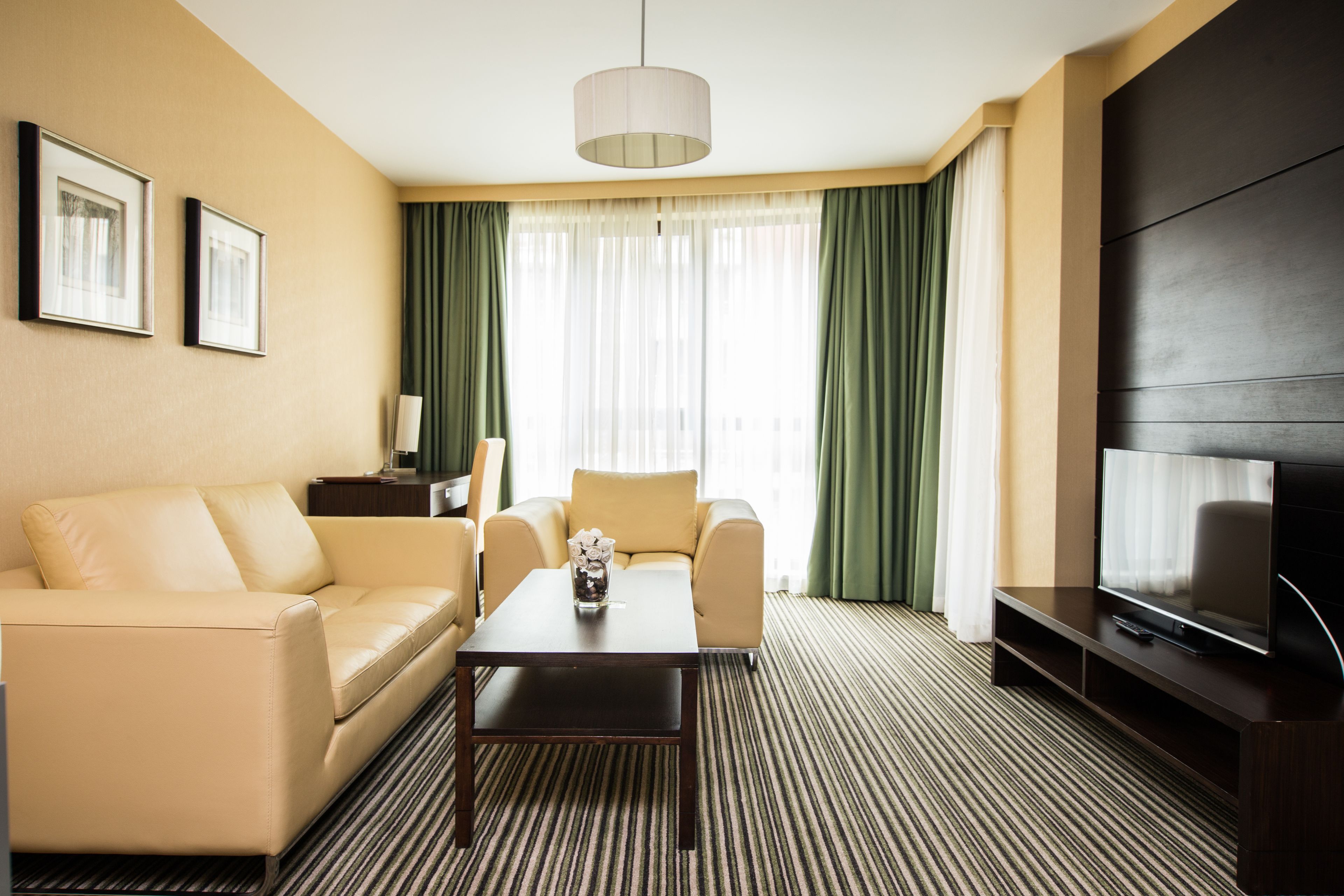 A hotel room with a sofa, a coffee table, a TV, and a large window with curtains.