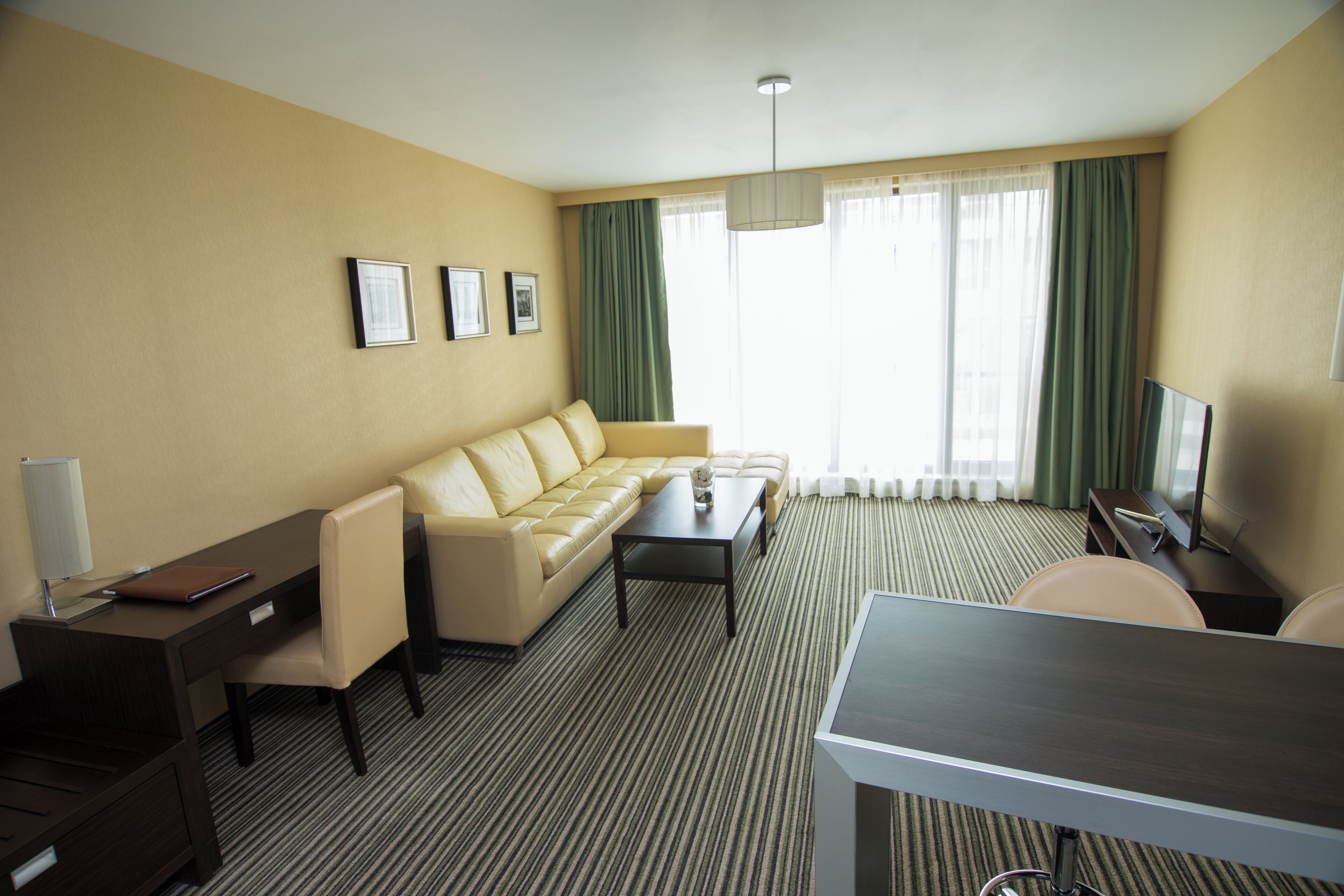 A hotel room with a sofa, a desk, a chair, a television, and a window with curtains.