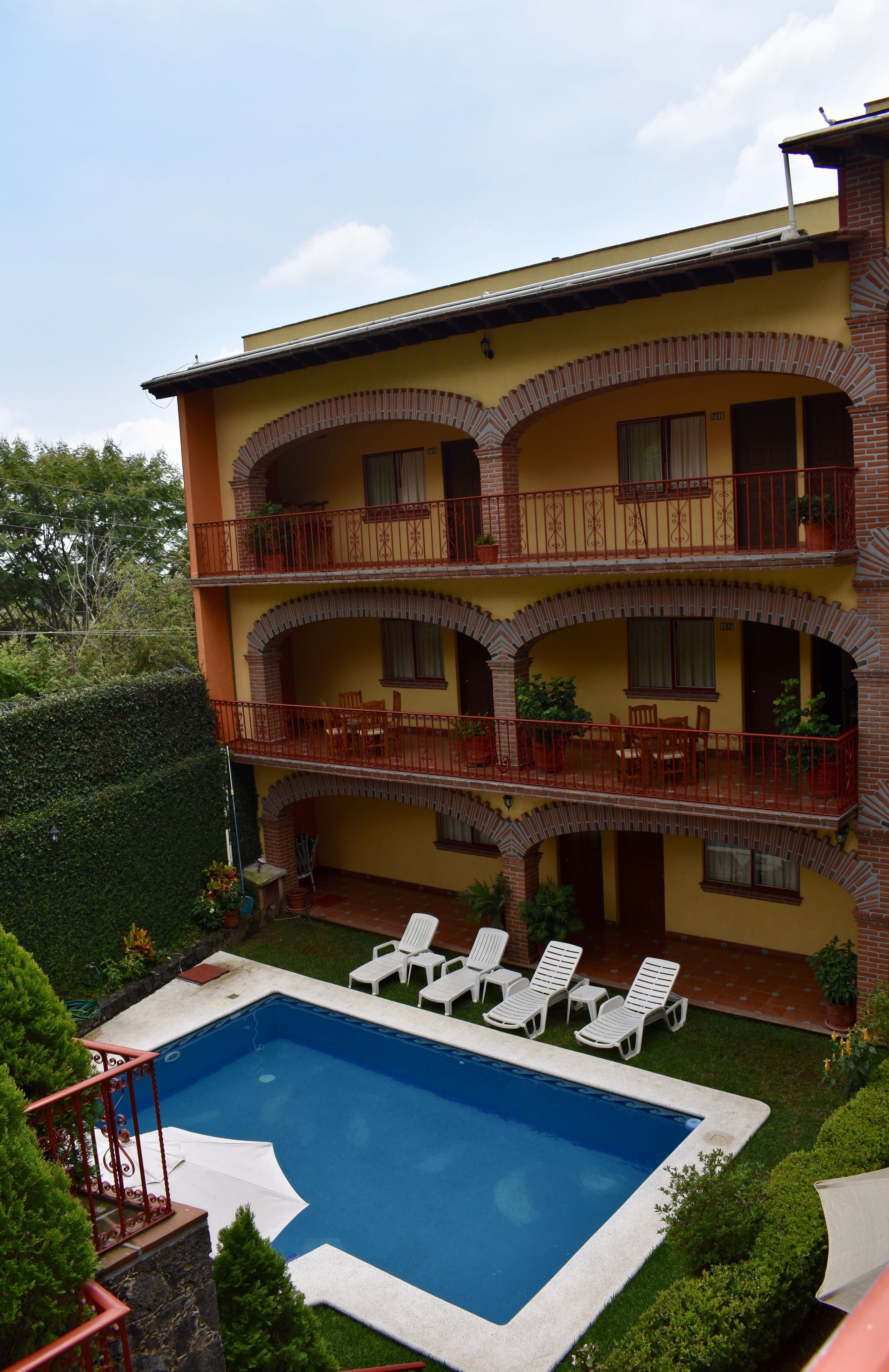 Un edificio de varios pisos con piscina, balcones con barandillas y zona de estar al aire libre.