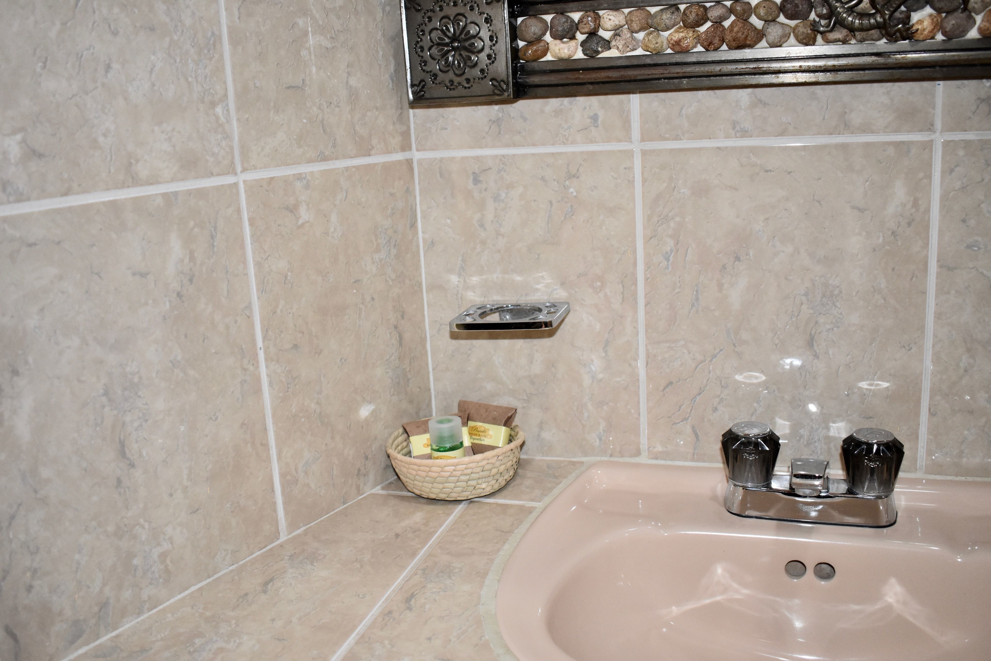 A bathroom with a beige tiled wall, a sink with two faucets, and a soap dish.