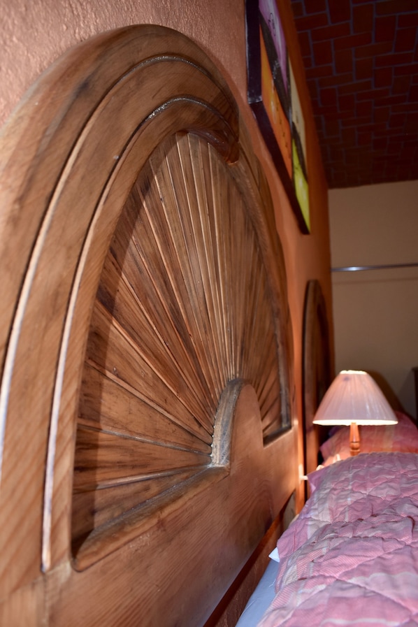 A wooden headboard with a fan-like design, a lamp, and a patterned bedspread.