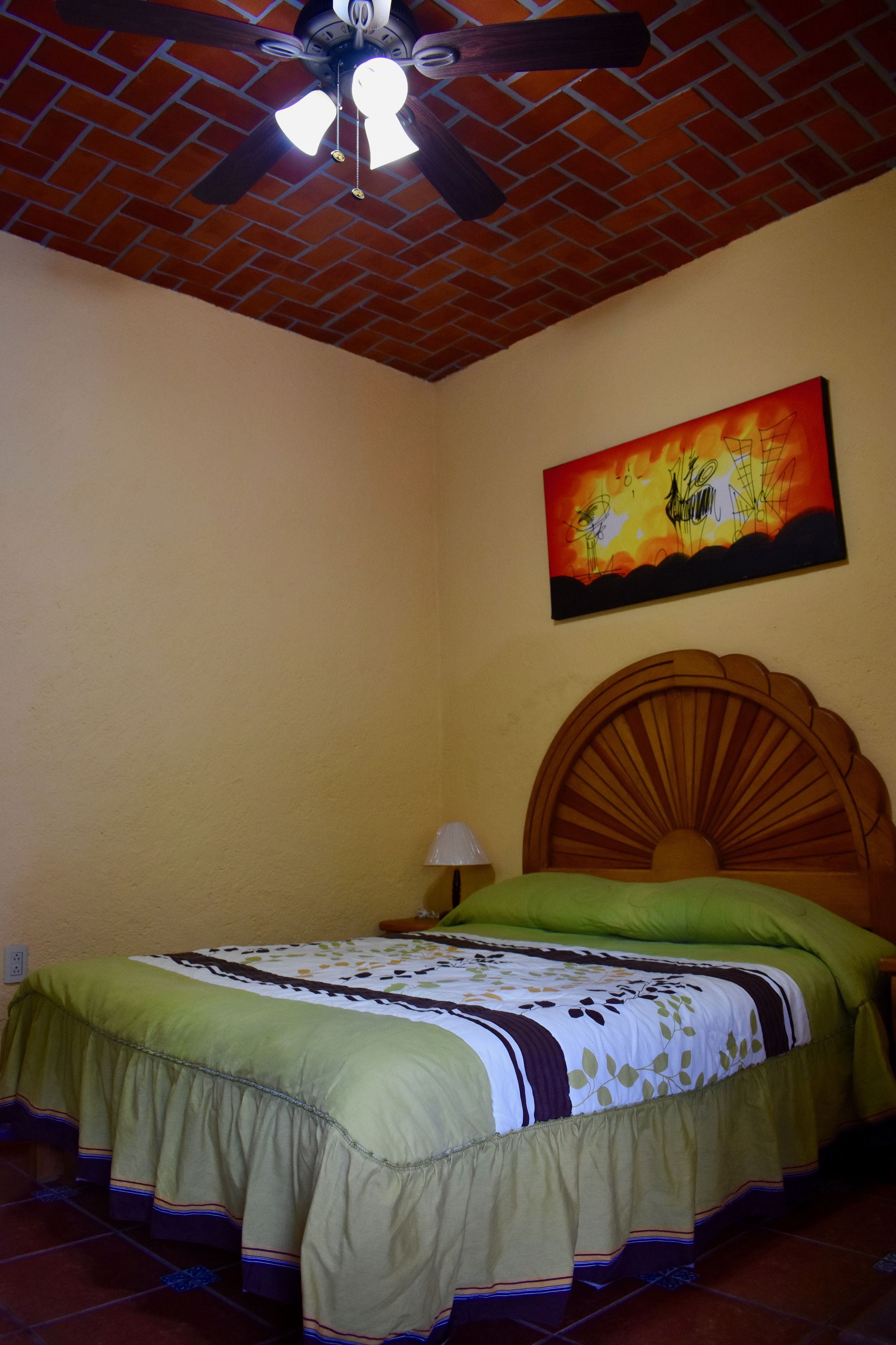 A bedroom with a brick ceiling, a wooden headboard, a green bedspread, and a painting on the wall.