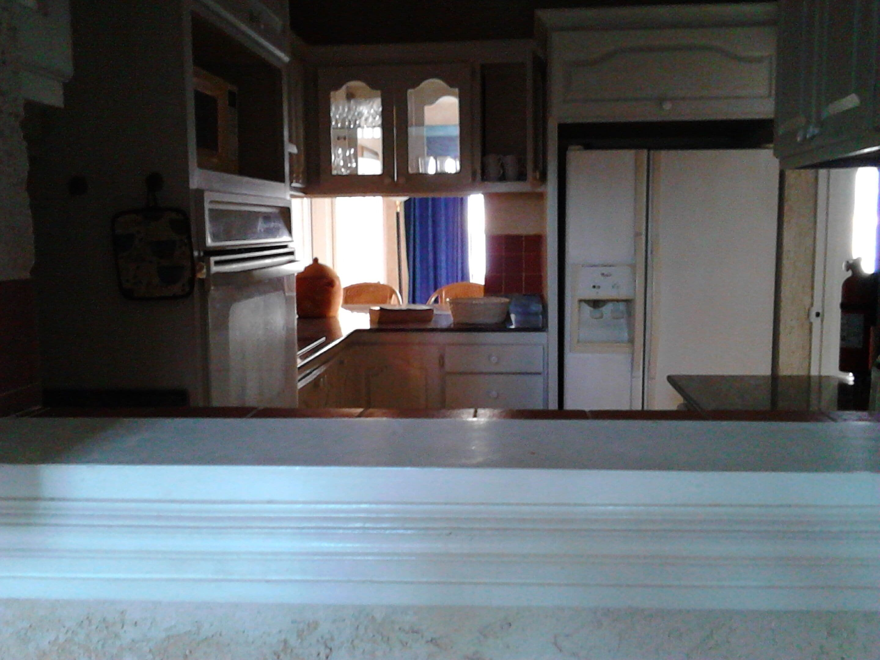 A kitchen with a refrigerator, oven, and microwave. There is a window with curtains and a sink with a mirror above it.