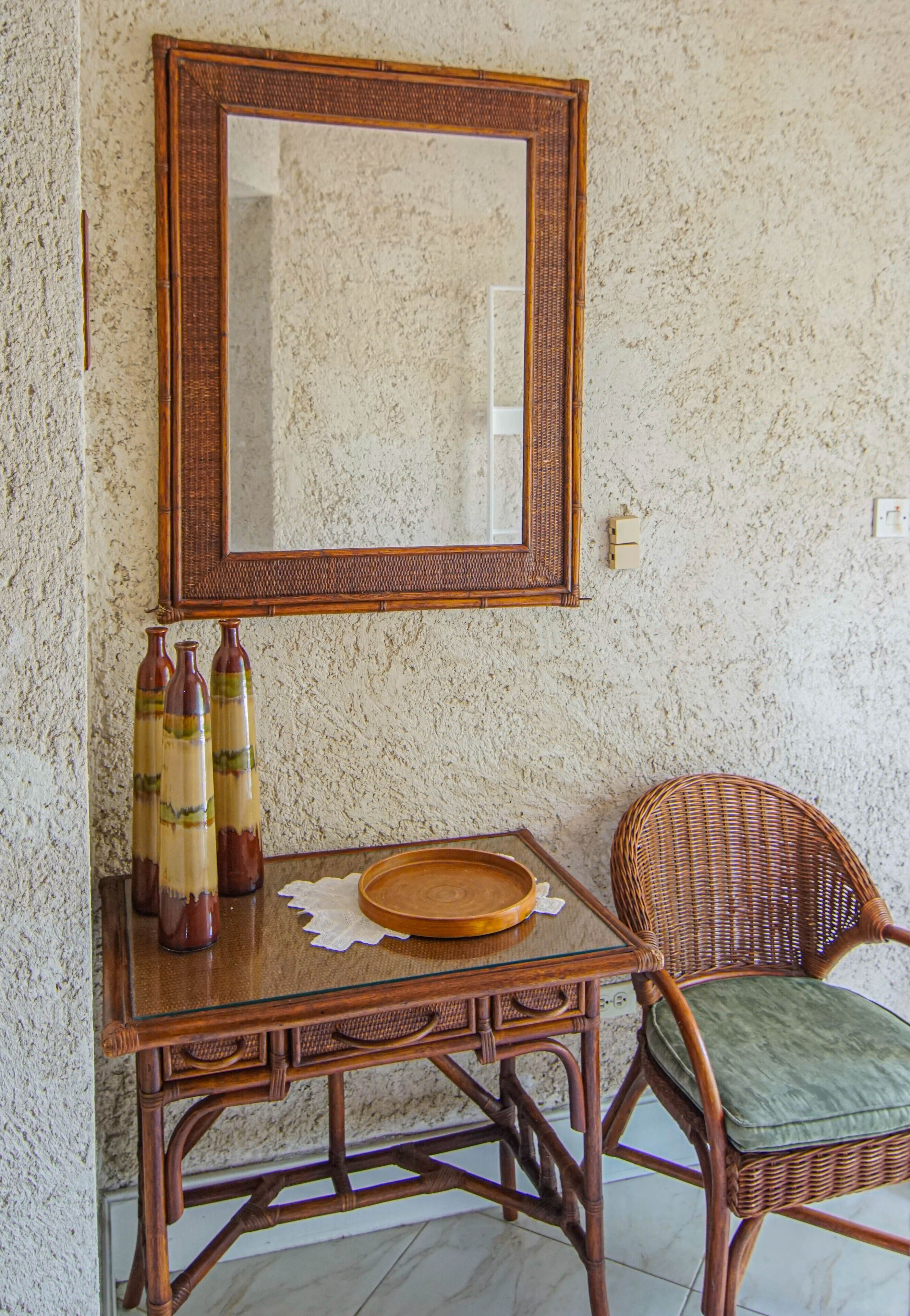 A wicker chair with a cushioned seat, a small wooden table with a tray, and three bottles on the table.