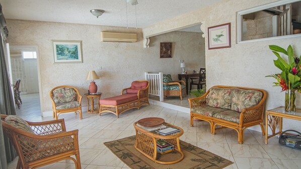 Una sala de estar con muebles de mimbre, una mesa de centro y un comedor al fondo.