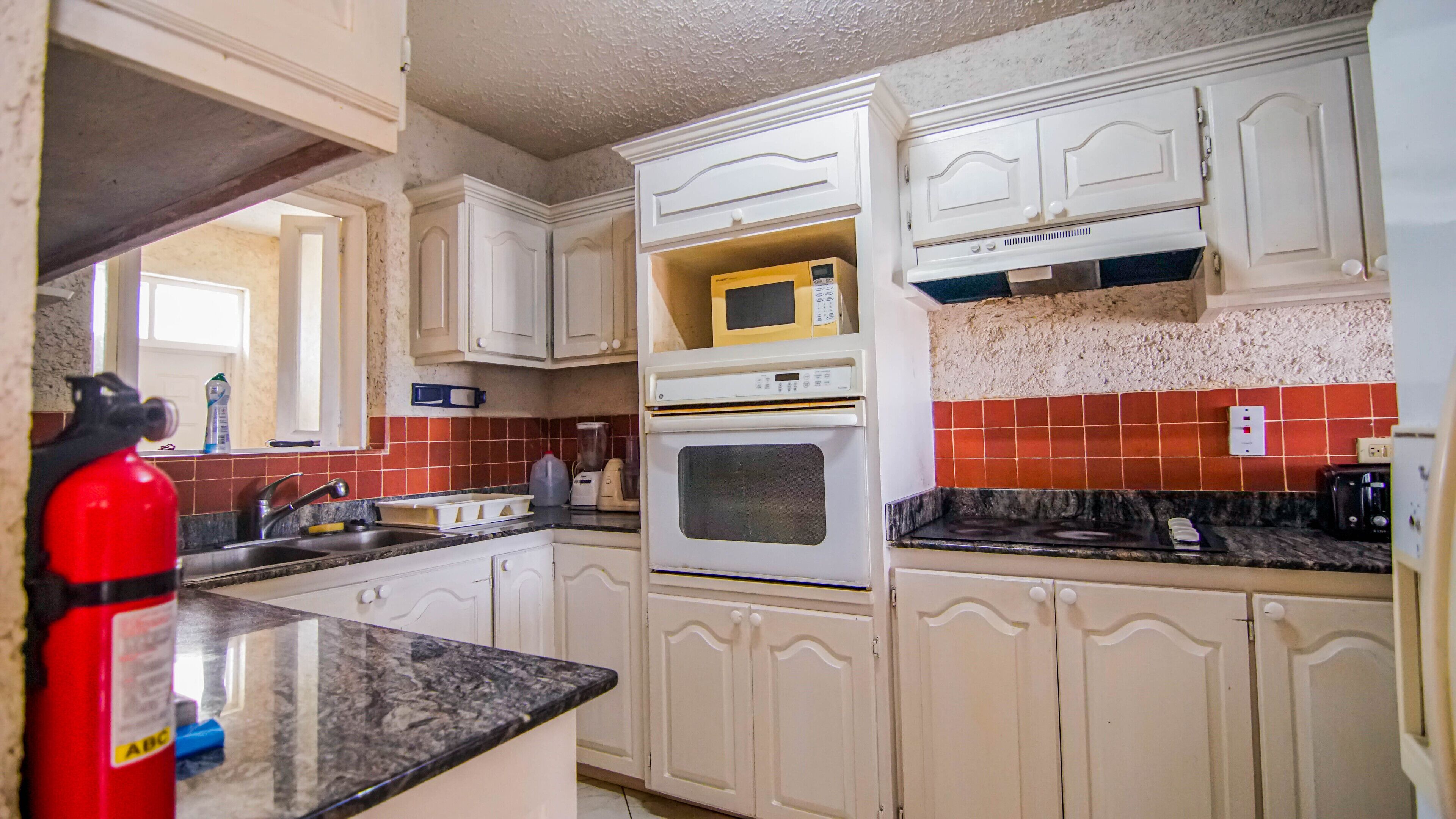 A kitchen with white cabinets, a microwave, an oven, a sink, and a red fire extinguisher.