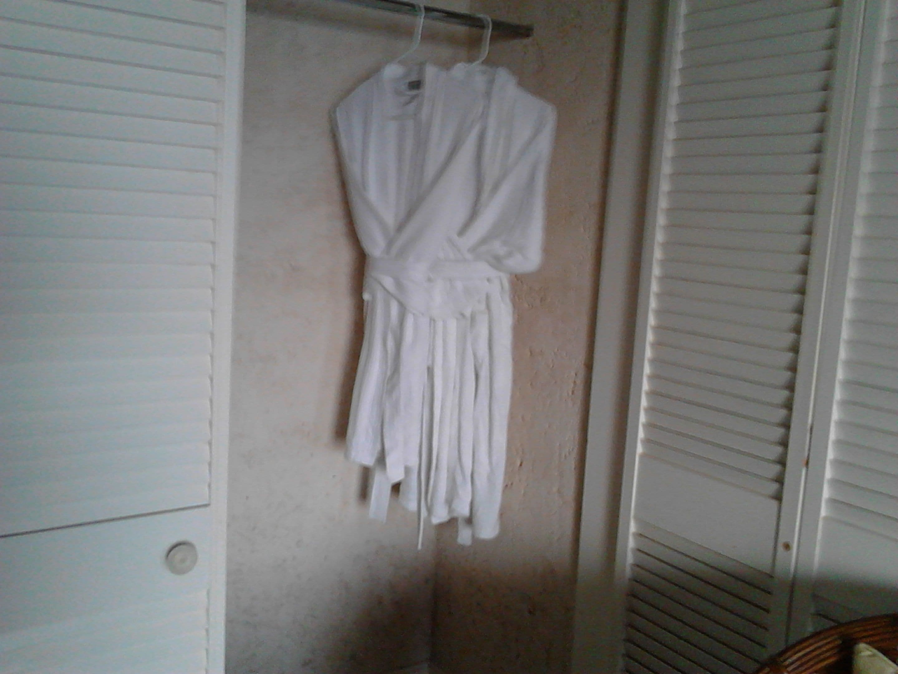 A white robe hanging on a wall in a room with a closet and a window with blinds.