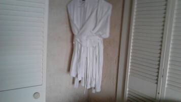 A white robe hanging on a wall in a room with a closet and a window with blinds.