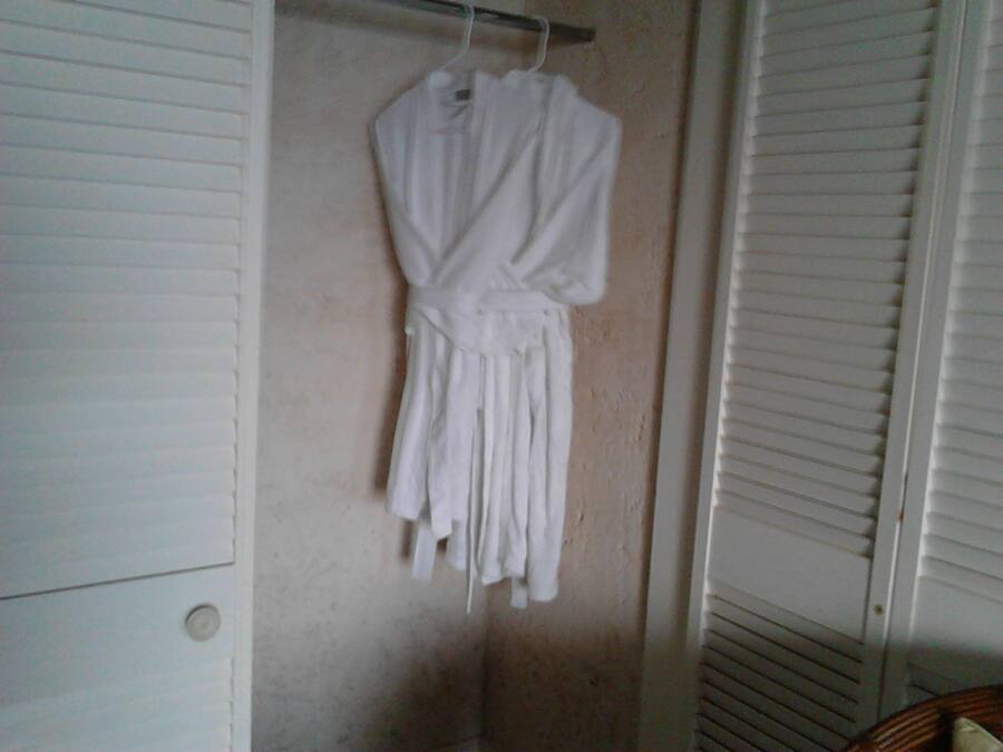 A white robe hanging on a wall in a room with a closet and a window with blinds.